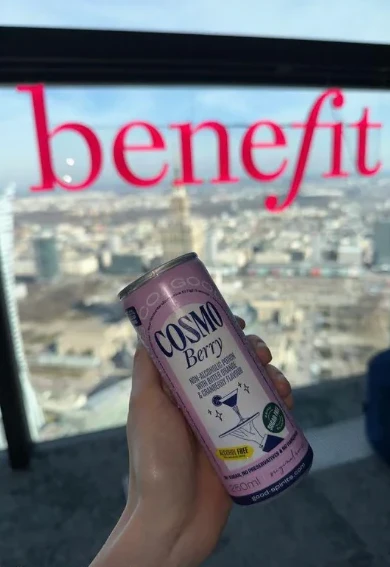 A hand holding a Cosmo Berry can against a city skyline at a rooftop event